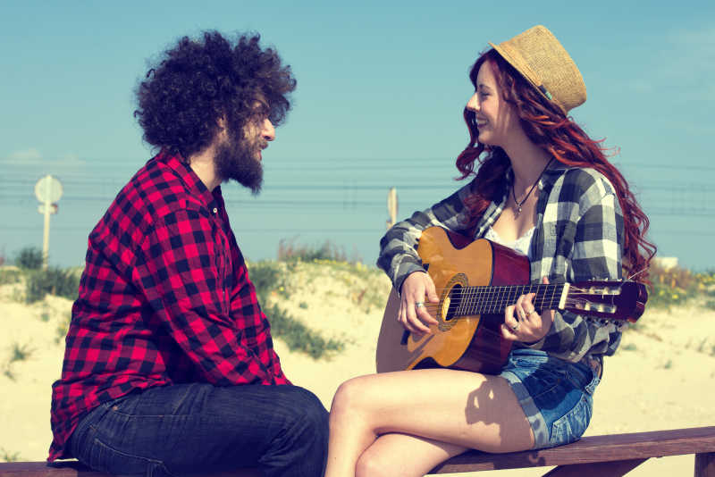 户外栏杆上一对年轻夫妇在弹吉他