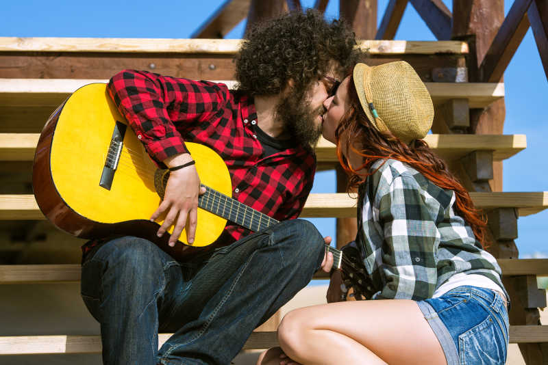 手拿吉他的男子和女友在台阶上接吻