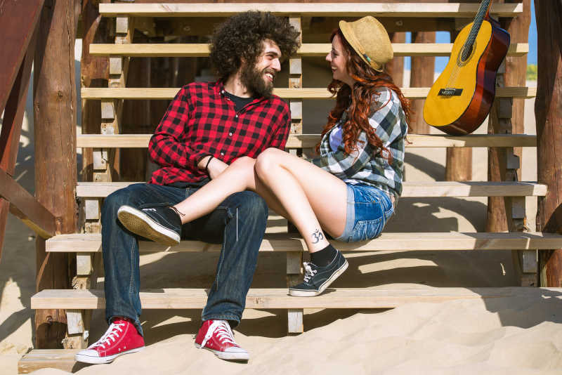 坐在木制台阶上的年轻夫妇身旁放着吉他