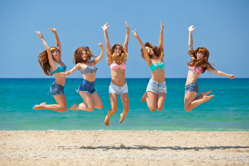 快乐放松的女孩们在海滩上跳跃