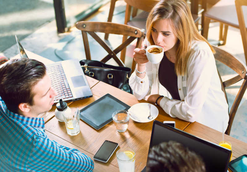 喝咖啡聊天的年轻人桌上放着笔记本电脑平板和手机