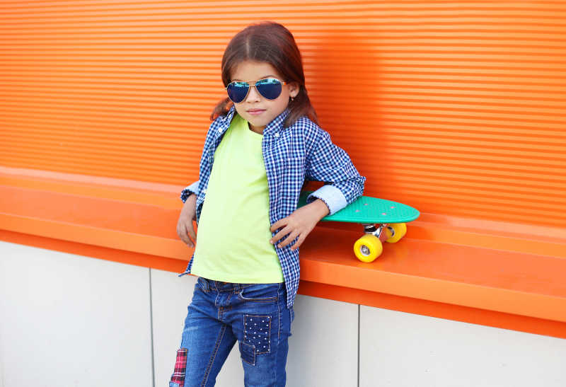 在橙色背景会玩滑板的时尚的女孩