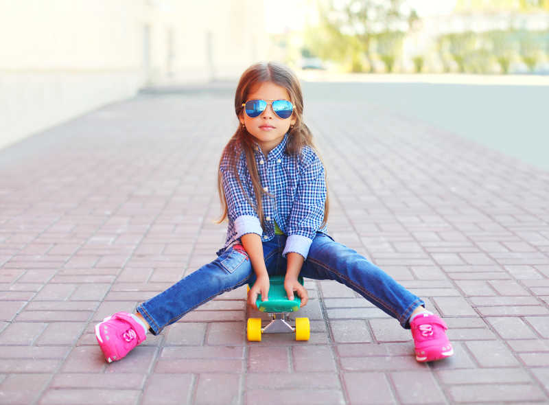 街头坐在滑板上的时尚小女孩