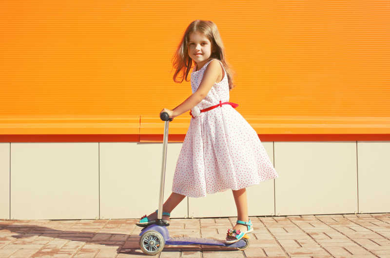橙色墙背景中玩踏板车的小女孩