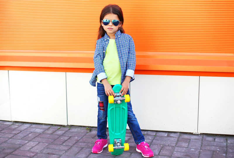 戴着太阳镜的和手拿滑板的时尚小女孩