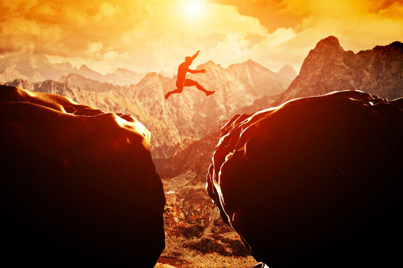 日落时在两座山峰之间跳过悬崖的人