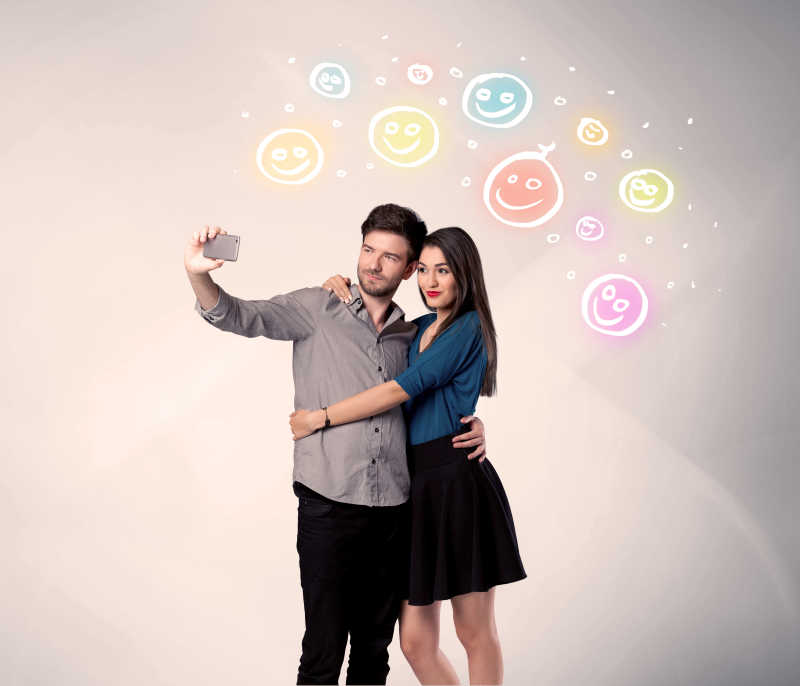 一个手机和多姿多彩的幸福笑脸图上面的概念采取selfie照片开朗的年轻夫妇