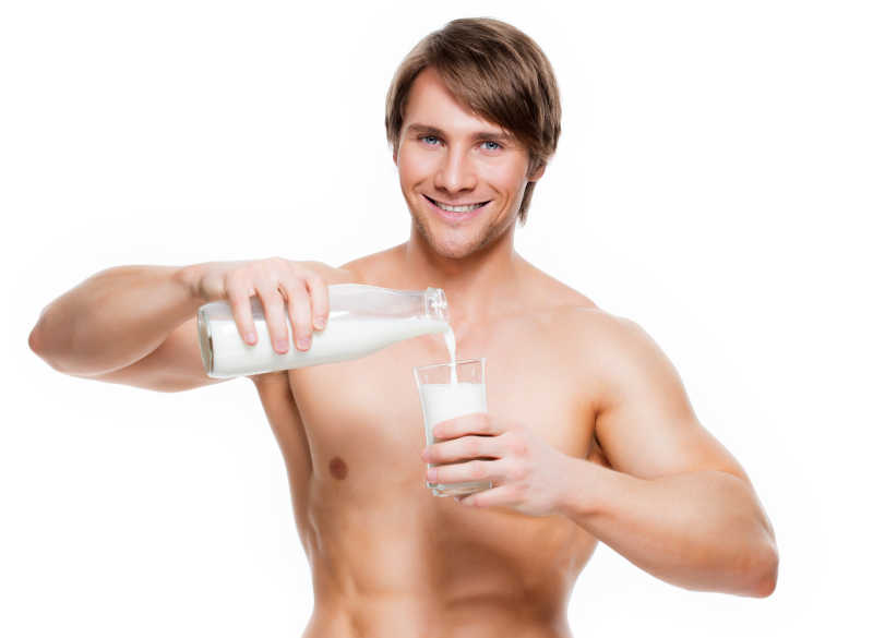 肌肉发达的年轻人正在往玻璃杯里倒着牛奶