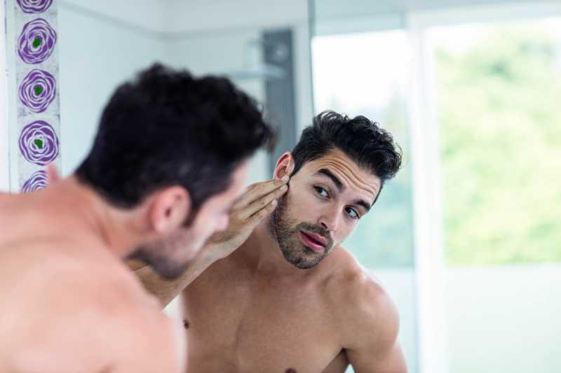 英俊的男人对着镜子刮胡子