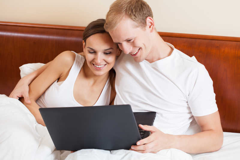 年轻夫妻在床上用笔记本电脑浏览信息