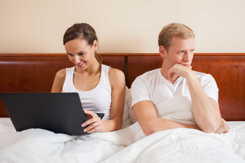 床上无聊的丈夫和一本正经操作电脑的妻子