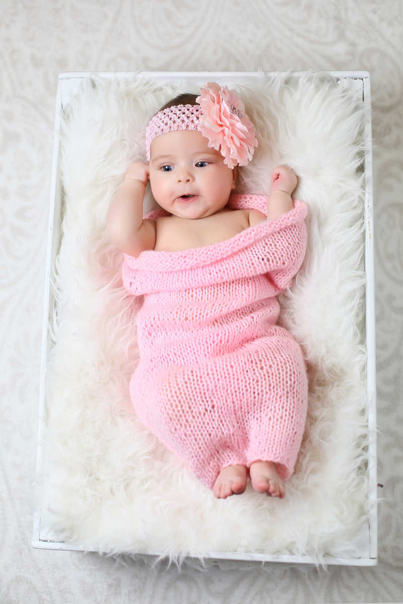 躺在白色毛毯上盖着粉色被子的可爱女婴
