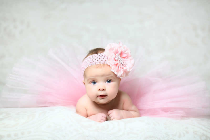趴在白色被子上的新生女婴带着粉色发卡