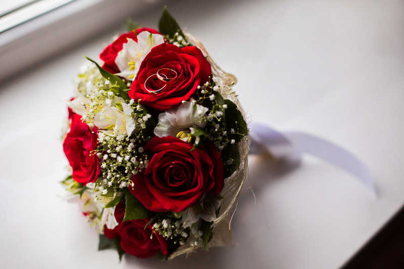 白色背景下一束白色的花和红玫瑰上的结婚戒指