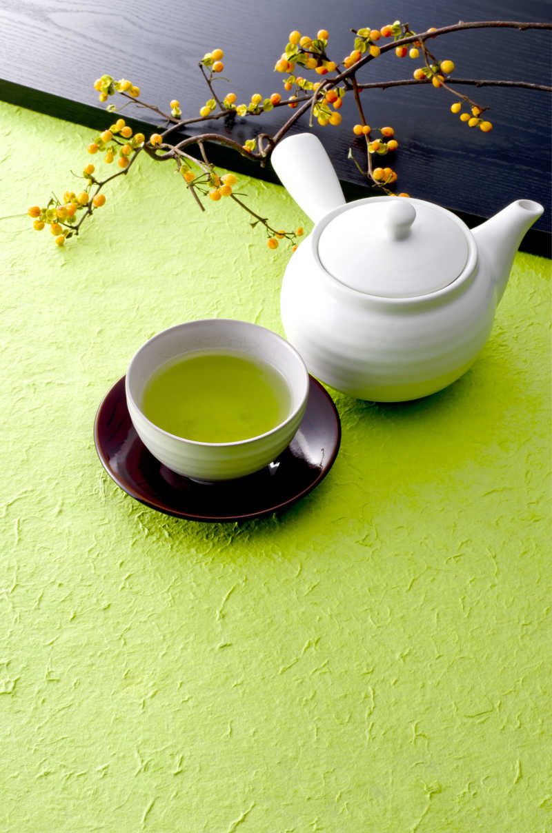 绿色背景中的白瓷茶壶和茶杯里的绿茶