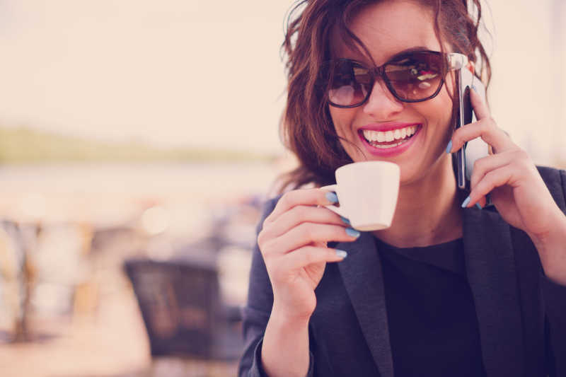 开心的年轻女孩一边喝咖啡一边用手机聊天