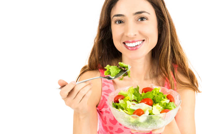 白色背景下微笑的女人吃蔬菜沙拉