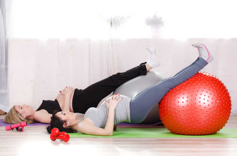 将腿放在健身球上练习瑜伽的两位孕妇