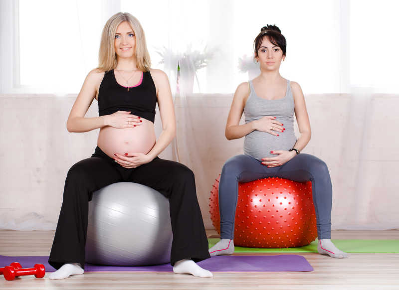 坐在瑜伽球上健身的两个孕妇