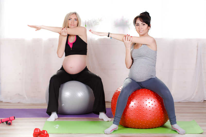 坐在瑜伽球上健身的金发和黑发孕妇