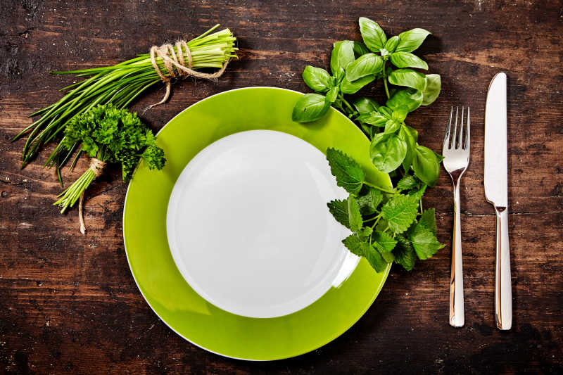 在木制桌上的新鲜健康的绿色草本和绿色板餐具