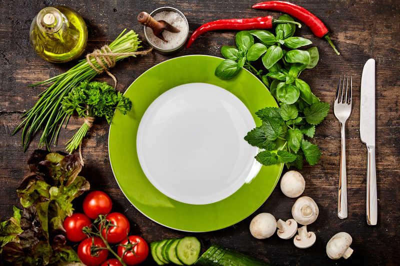 木制餐桌上有各种新鲜药草和健康生蔬菜的绿色和白色刀叉