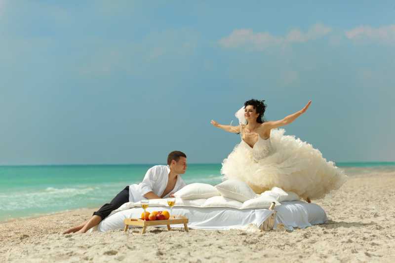 沙滩上幸福的新娘在床上向丈夫飞翔