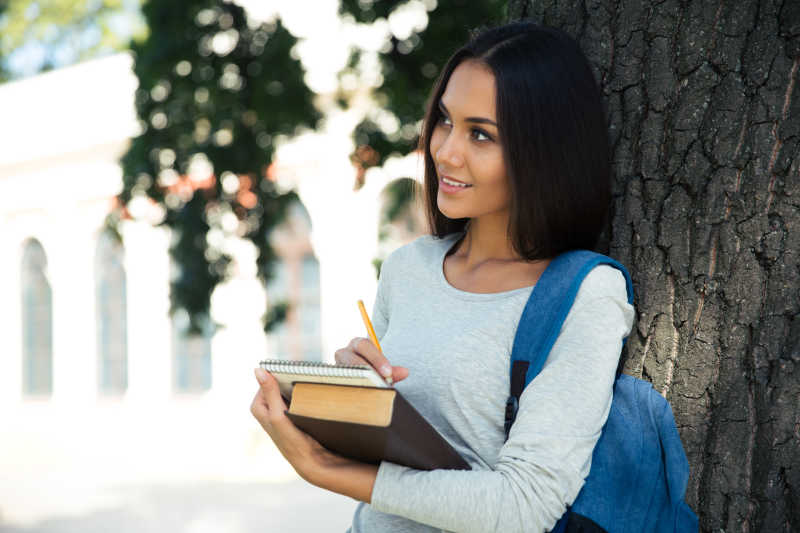 树下正在微笑做笔记的女学生