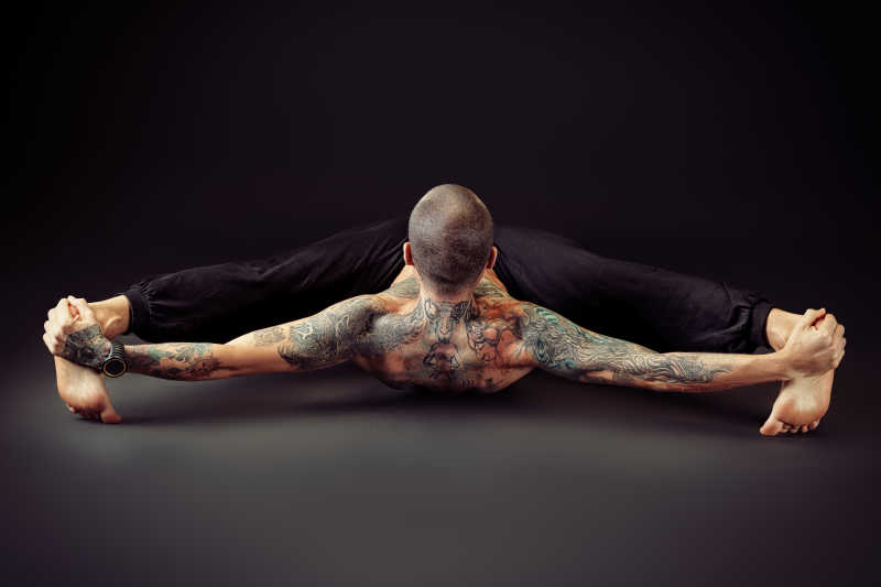 黑色背景下有纹身的男人在做高难度的瑜伽
