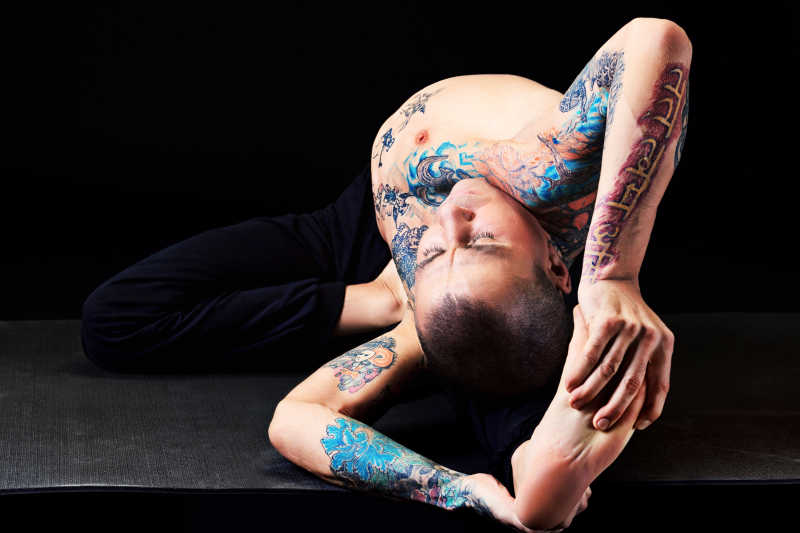 纹身的男人抱着脚在做瑜伽练习