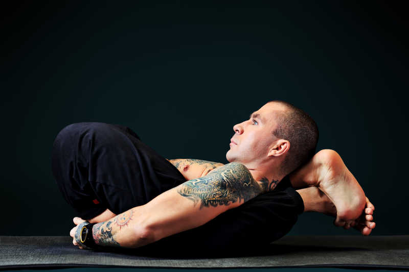 黑色背景下纹身的男人在做高难度的瑜伽