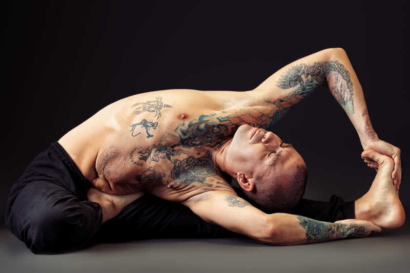 有纹身的男人躺在腿上在练习瑜伽