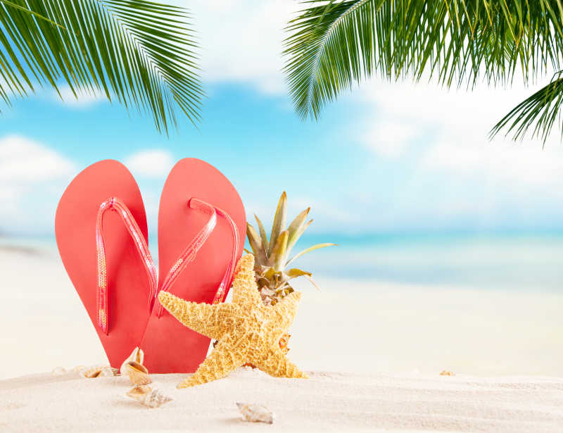 背景模糊的夏日沙滩上的鞋子和贝壳