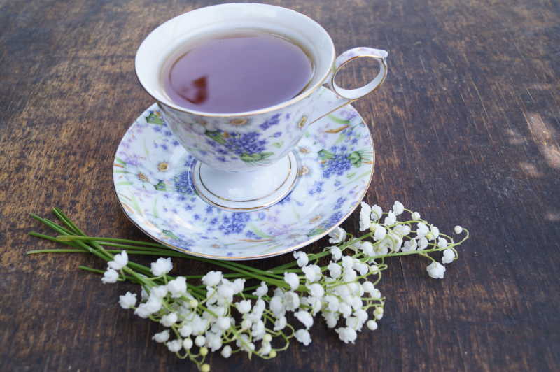 木桌上的装着茶水的茶杯和铃兰花
