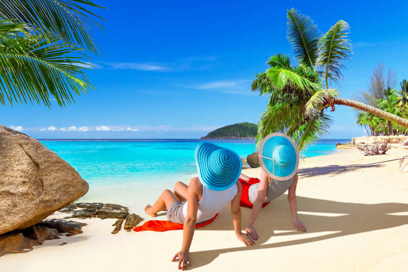 两位戴帽子的妇女在海滩上沐浴阳光