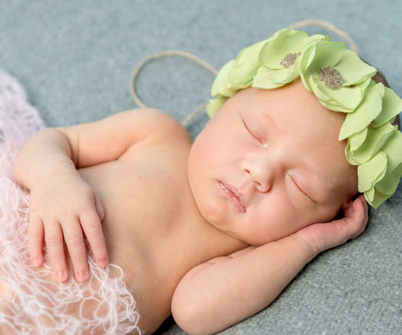 毛毯上头枕花圈的可爱的初生婴儿
