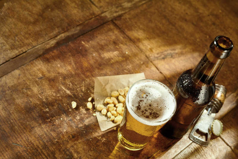 在老旧的木桌上的用起子起开的一瓶啤酒和花生