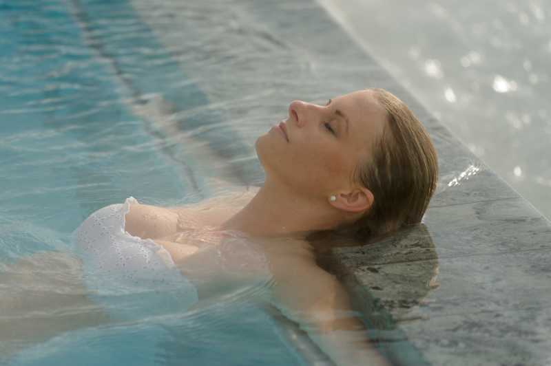 年轻的金发女子躺在泳池边上休息