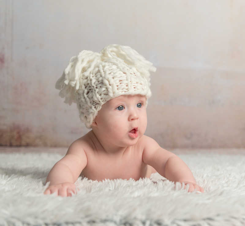 趴在毛毯上戴着针织帽的婴儿