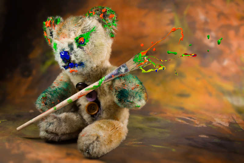 拿着飞溅的画笔的彩色玩具熊