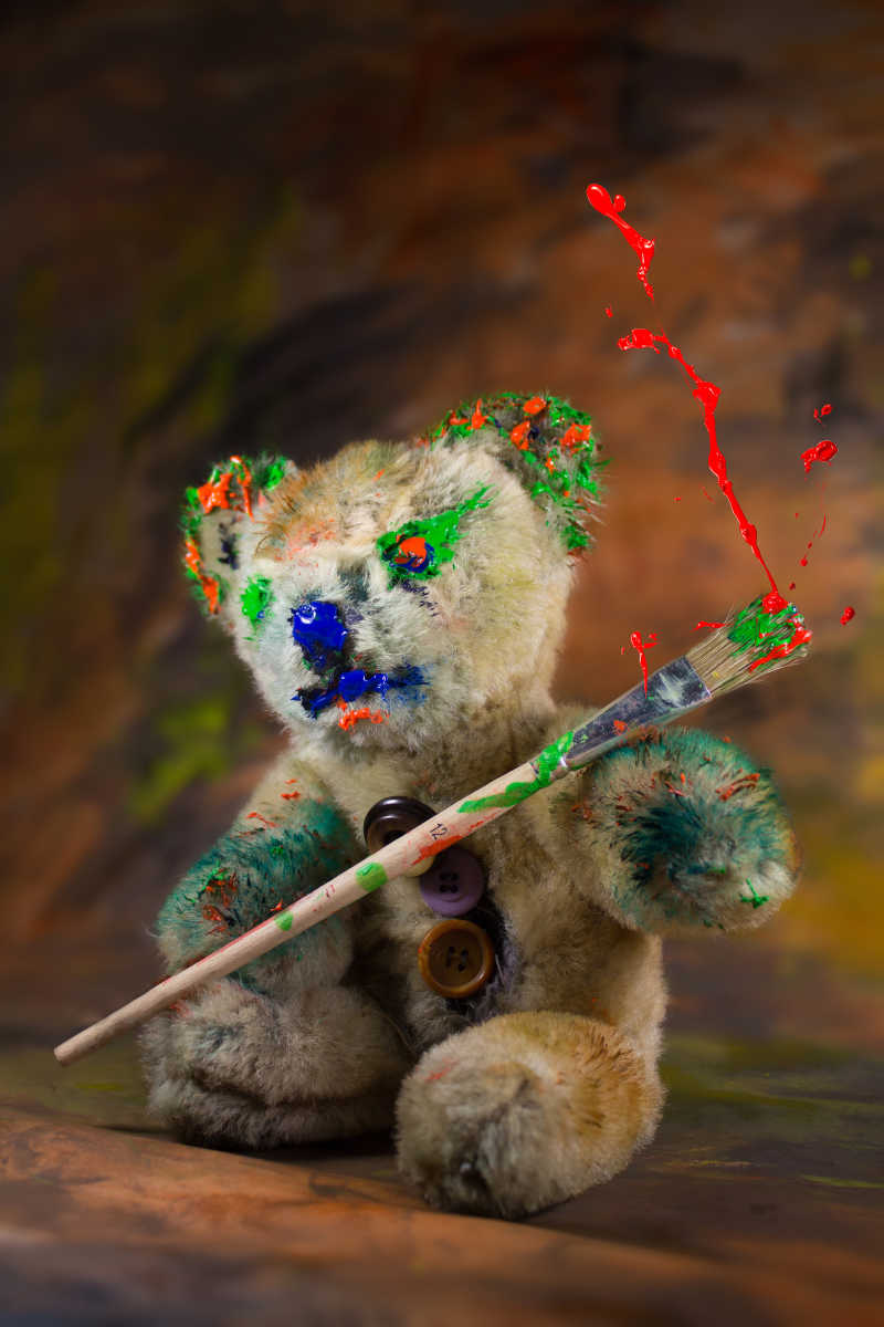 沾染颜料的玩具熊拿着画笔