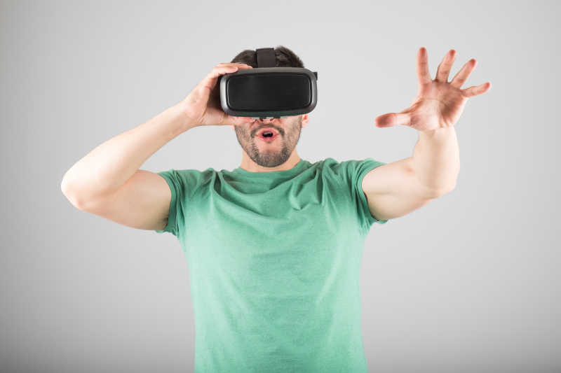 灰色背景前带着3D虚拟眼镜的男人伸手去触摸空中