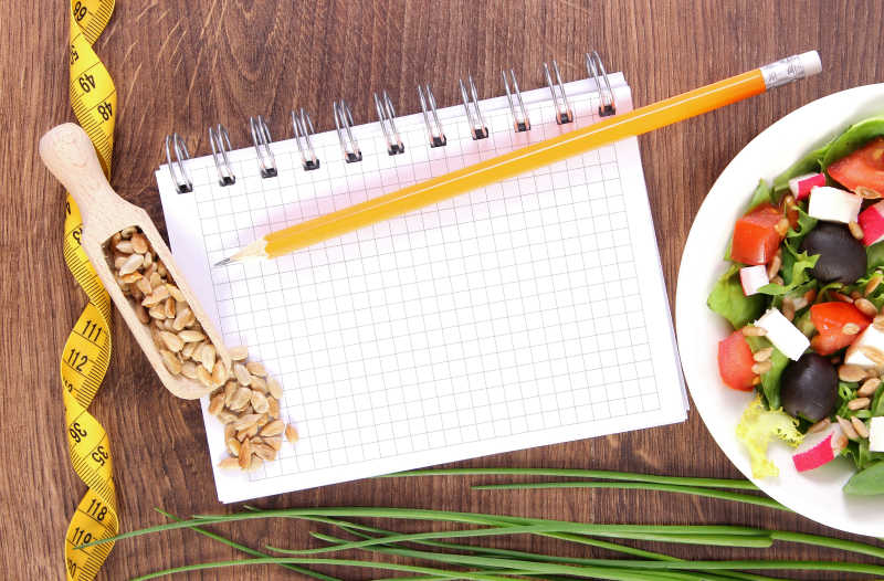 桌子上的蔬菜沙拉和笔记本皮尺减肥概念