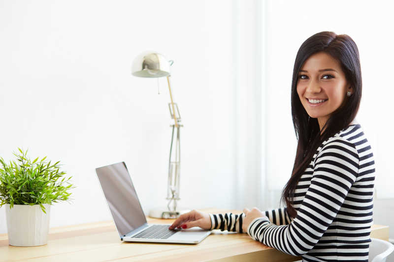 面带微笑的女人坐在办公桌前在用手提电脑办公