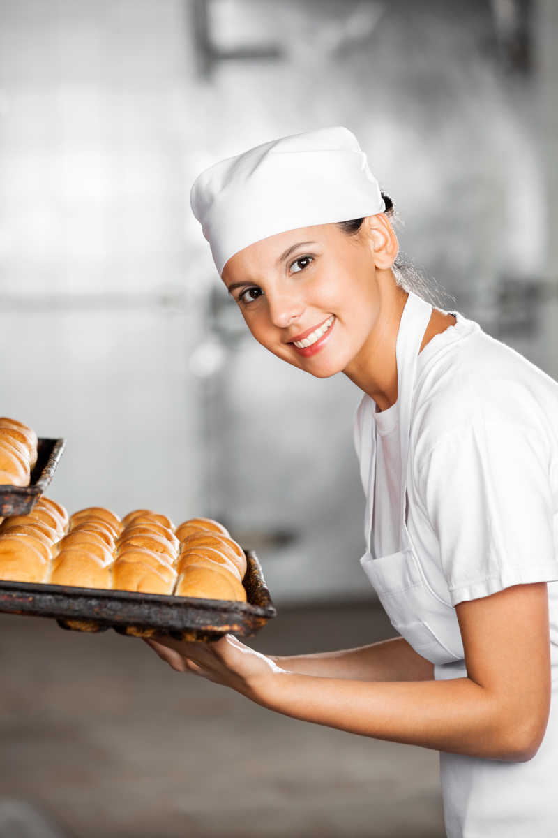 模糊背景下拿着面包托盘的美女面包师