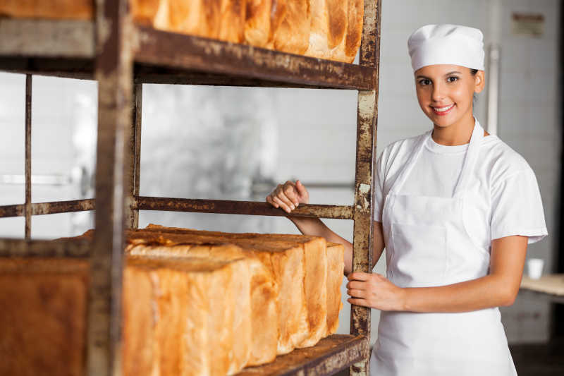 站在面包架旁微笑的美女面包师