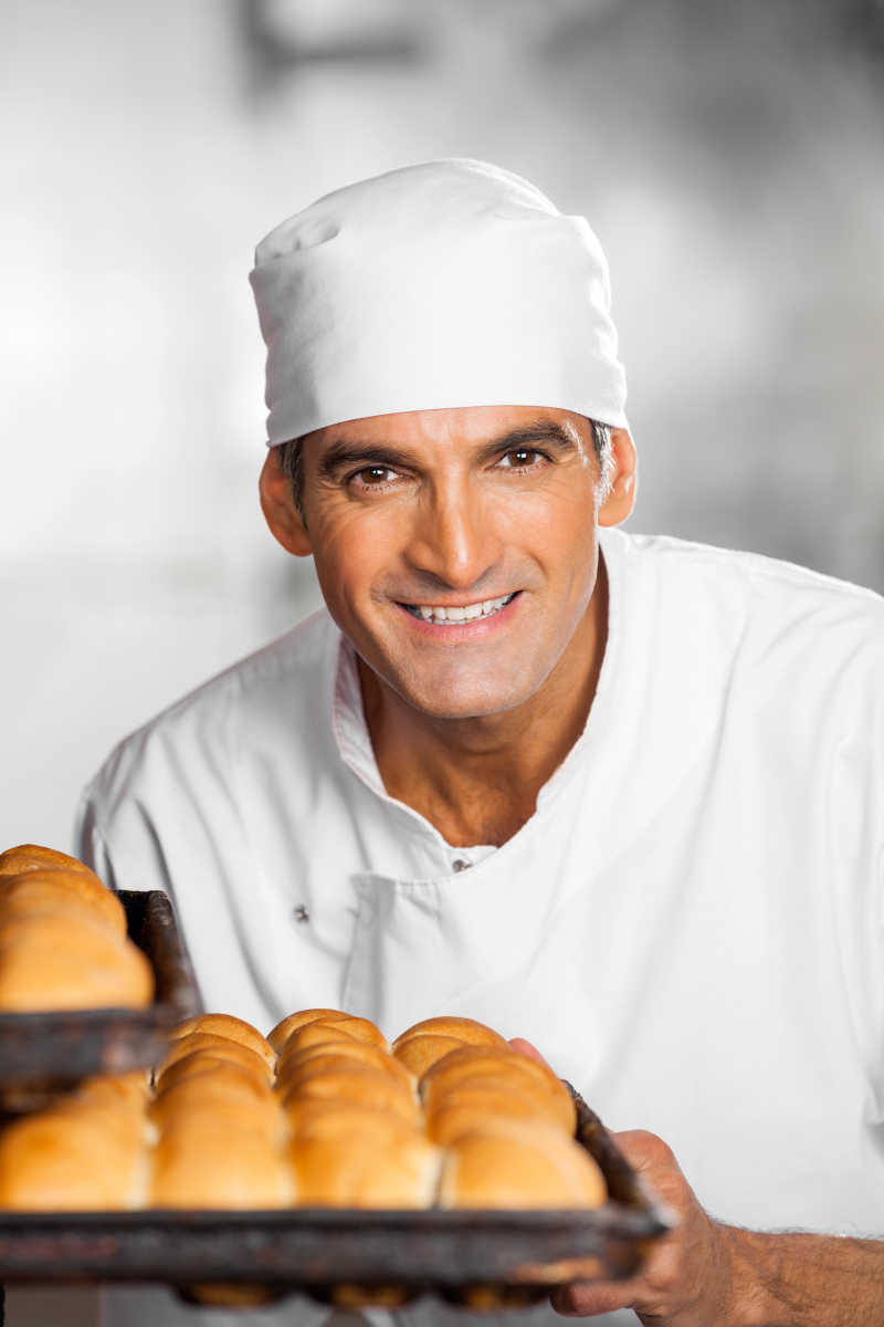 灰色背景下的拿着面包托盘的男烘烤师