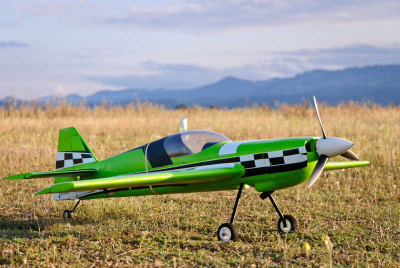 群山背景下停在黄色草地上的绿色飞机模型