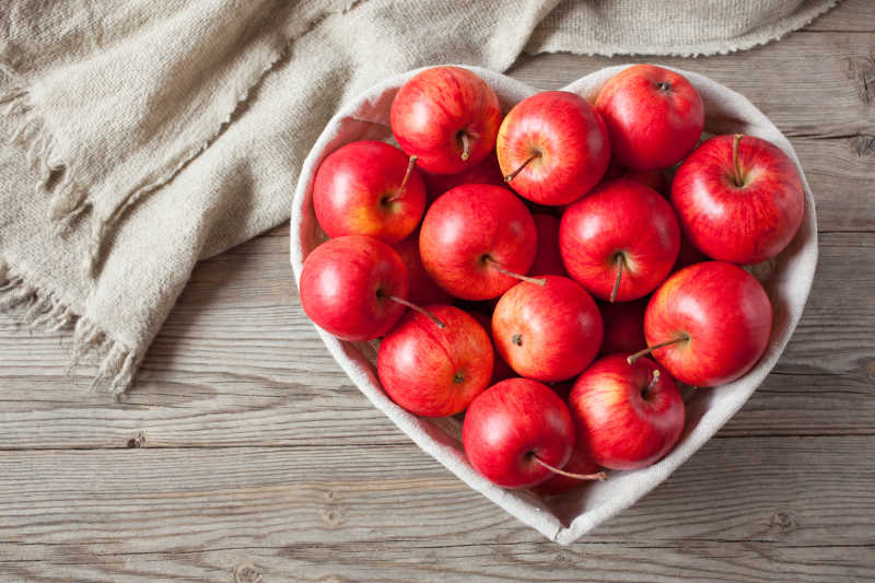 木桌上放在心形盆子里的红色苹果