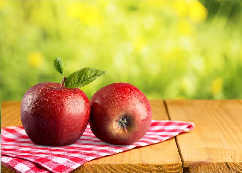 木桌上红餐布上的红苹果